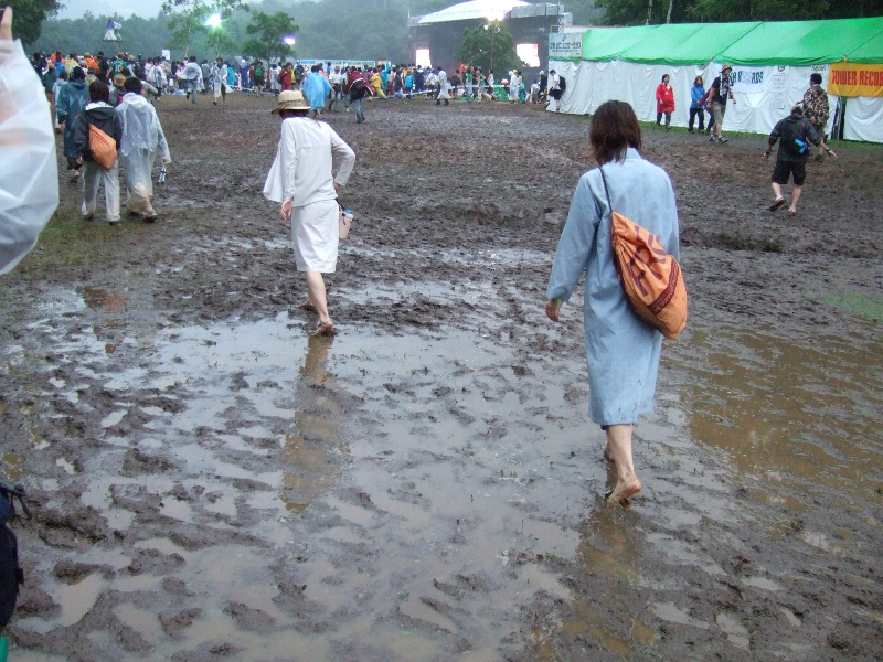 グリーン・ステージとアーティスト・グッズ売り場の間。3日目は通行禁止になりました。女性が靴を手に持ち、はだしで歩いています。2日目午後6時半ごろ。