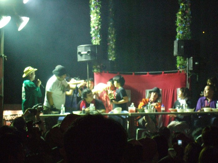 レッドマーキーで前夜祭公演が行われている間、お立ち台（というのか？）で早食い競争が行われます。何を早食いするかは年によって変わります。参加は自由です。