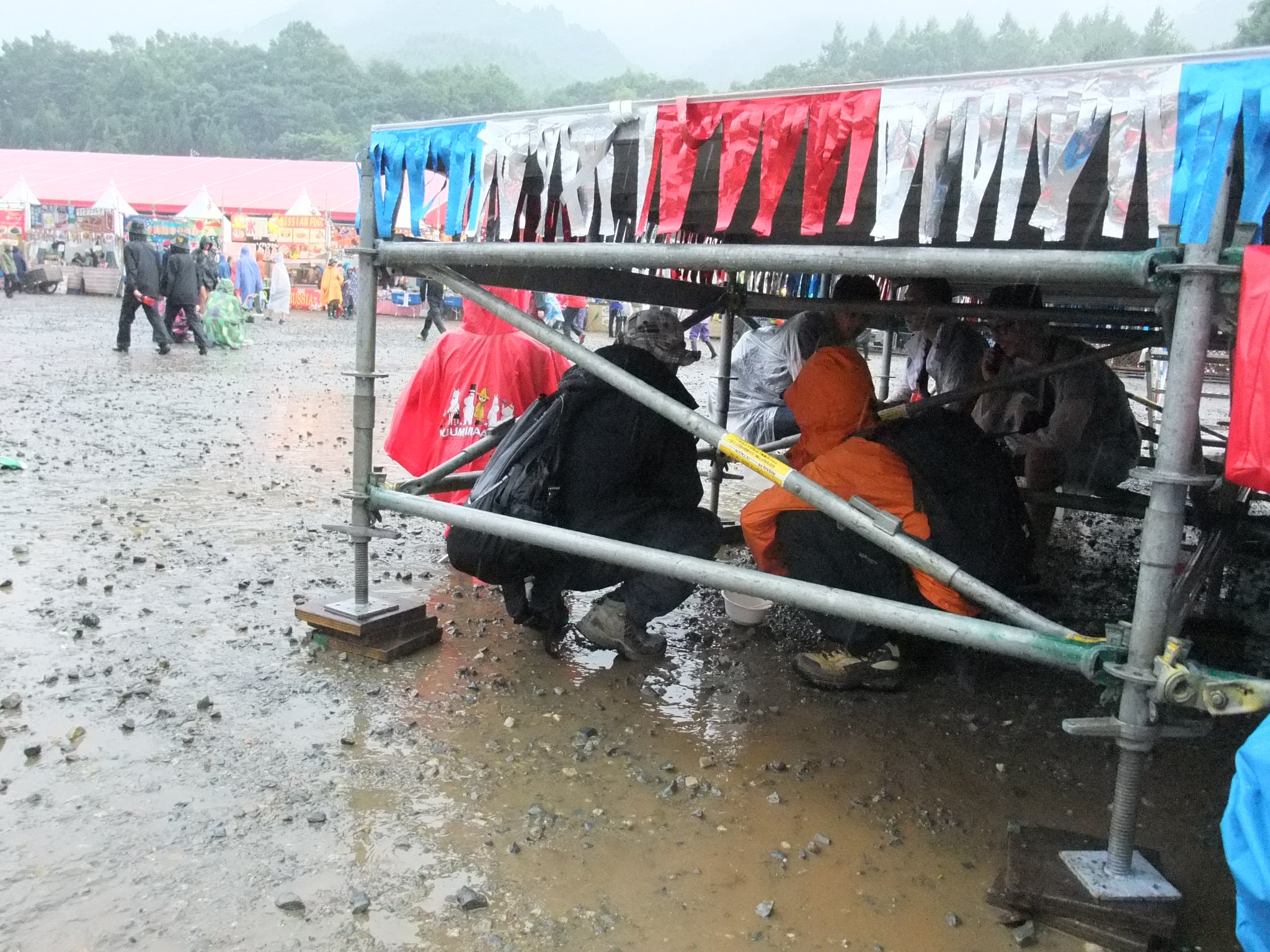 雨が降って櫓の下にもぐる人。