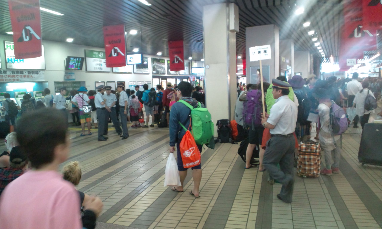 越後湯沢駅。新幹線の乗車券の行列ができていて、駅員が「最後列」の案内をしています。