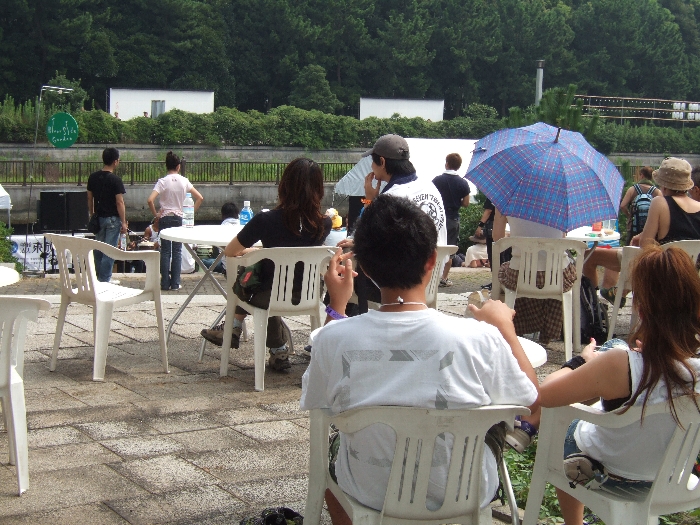 いす、テーブルがあり、近くには飲食店もあります。対岸の右に見えるのは取り付け途中の提灯。