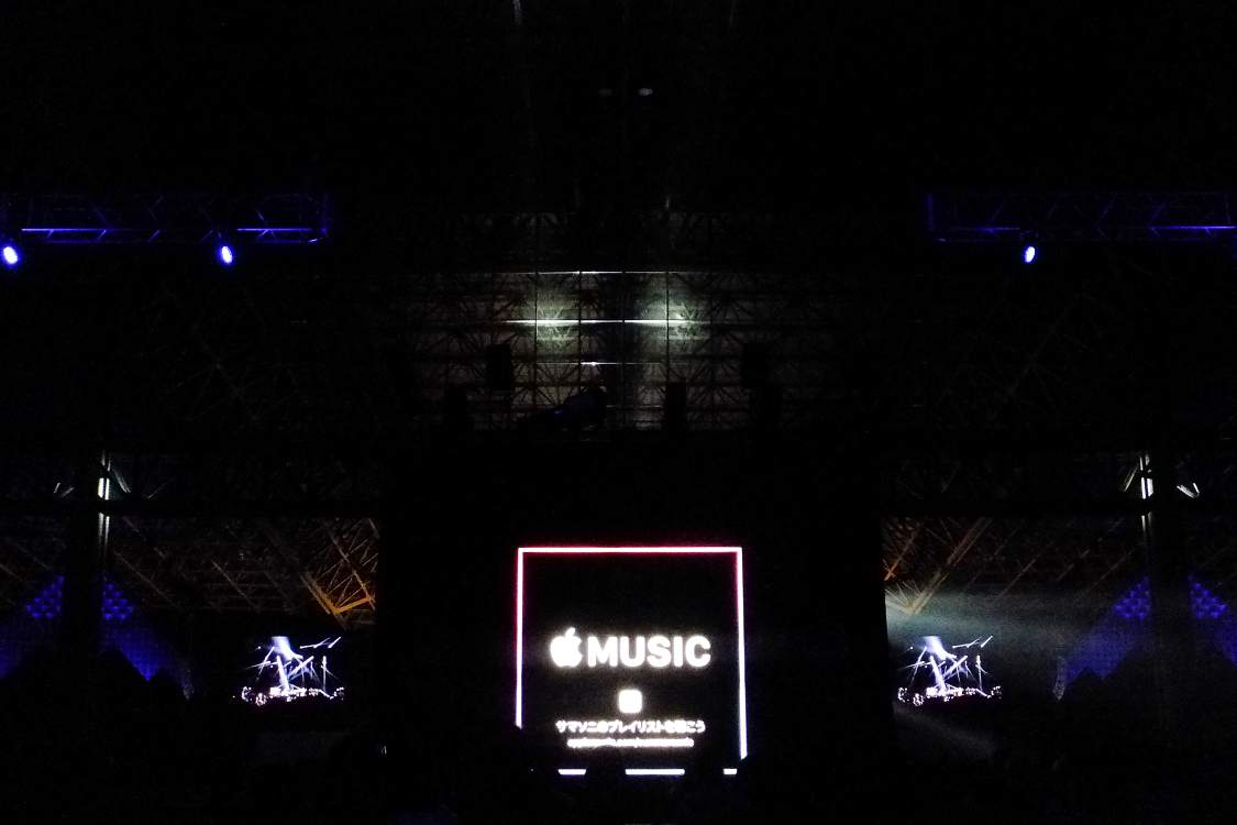 ステージ向かいにあるアップルの宣伝。両側に見えるのはステージの左右にあるモニターの画面。